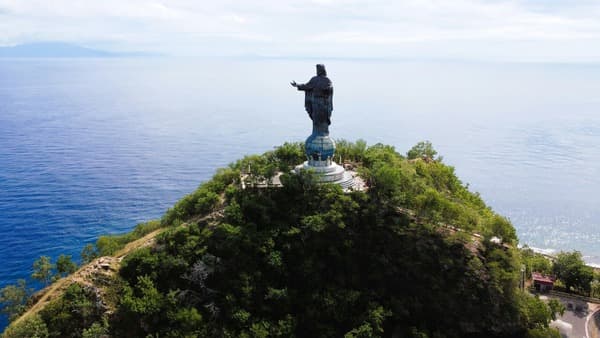 Aerial view of the Cristo Rei statue standing on a green headland above deep blue water.